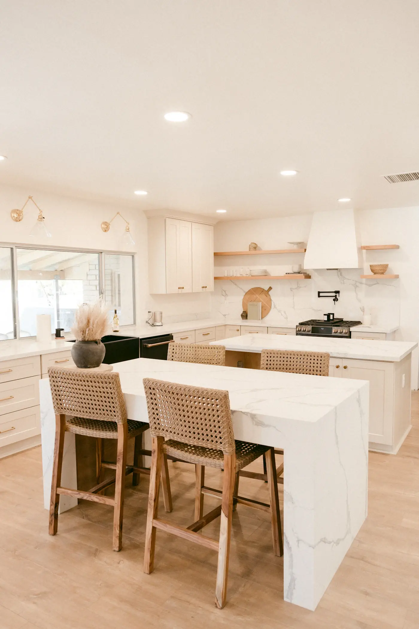 Renovated kitchen with white marble island, woven stools, and wood floor